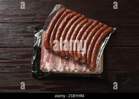 Packungen trockener geräucherter Würstchen und geschnittenem Speck auf Holztisch, Blick von oben Stockfoto