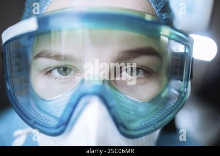 Arzt mit chirurgischer Schutzbrille und Maske in einer blau gefärbten Umgebung, aufmerksam im Gesundheitswesen Stockfoto