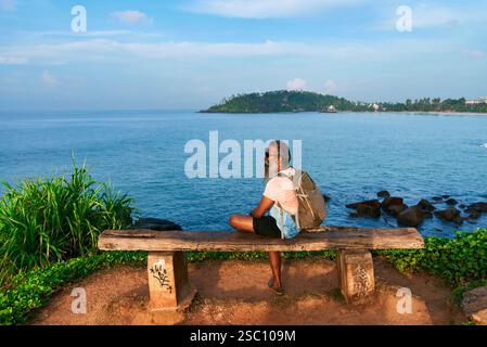 Bärtiger Seniorenmann mit Rucksack entspannt sich auf der Bank am Meer. Er betrachtet Natur und Leben. Die Szene deutet auf Reisen, Reflexion hin. Ideal für Themen von Stockfoto