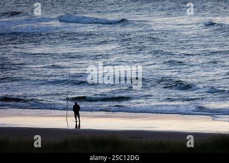 Silhouette eines Fischers, der bei Sonnenaufgang am Strand vor dem Meer steht Stockfoto