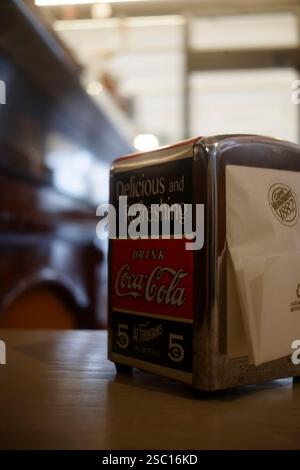 Cremona, Italien - 30. Januar 2025 Eine Nahaufnahme eines Coca-Cola-Serviettenhalters aus Metall mit Retro-Design und Werbung. Der Hintergrund ist Stockfoto