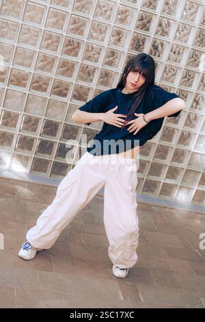 Die junge Tänzerin spielt an einem sonnigen Sommertag in lässiger Streetwear ausdrucksstarke Bewegungen in urbaner Umgebung Stockfoto