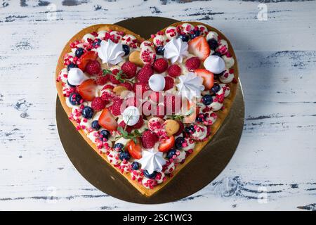 Eleganter herzförmiger Kuchen mit frischen Beeren, Creme und einer glänzenden Glasur. Romantisches Dessert für Valentinstag, Hochzeiten oder andere besondere Gelegenheiten Stockfoto