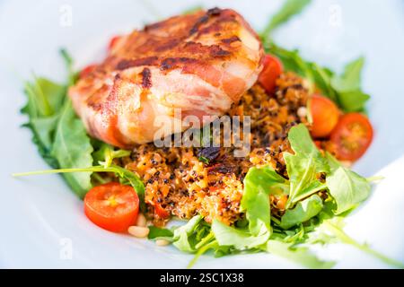 Nahaufnahme von Burrata in knusprigem Speck, serviert auf einem Bett aus Quinoa, Rucola und Kirschtomaten. Stockfoto