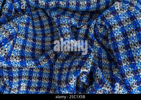 Eine Nahaufnahme aus gefaltetem boucle-blauem und schwarzem kariertem Material mit detaillierter Textur und weichen Falten. Stockfoto