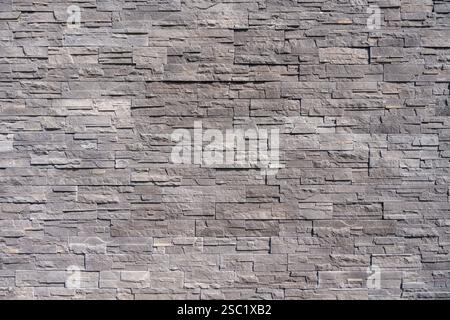 Eine detaillierte Ansicht einer modernen grauen Steinmauer mit rechteckigen Mustern und rauer Textur. Stockfoto