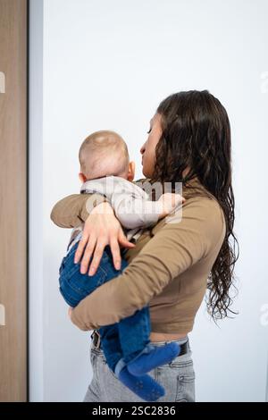 Mom nimmt ihren Kleinkind-Sohn um, während sie im Wohnzimmer steht Stockfoto