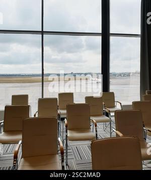Leere Stühle im VIP-Terminal des Regionalflughafens. Wartende Lounge mit Blick auf den Flugplatz, ein weißer Businessjet parkt in der Ferne. Stockfoto
