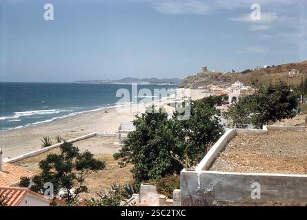 Torreblanca, Spanien. Anfang der 1960er Jahre – Blick auf eine Playa de Torreblanca in der Nähe von Fuengirola in der Provinz Málaga, Andalusien, Spanien. In der Ferne ist ein Wachturm zu sehen, der Anfang der 1970er Jahre abgerissen wurde, um Platz für die Hotelentwicklung zu schaffen. Ebenfalls zu sehen ist die „Osborne Bull“-Plakatfigur, die für die Werbung für den Brandy de Jerez der Osborne-Gruppe errichtet wurde. Stockfoto
