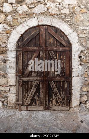 Alte dunkelbraune Holztür mit Bogen ist in einer alten Steinmauer, Hintergrund Foto Textur, Vorderansicht Stockfoto