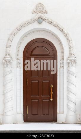 Eine alte Holztür ist in einer weißen Wand einer alten Kirche, Vorderansicht, Hintergrundfotos Stockfoto