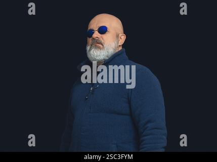 Bärtiger, kahler, brutaler Mann in dunkelblauem Pullover und Brille. Blick auf die Seite. Schwarzer Studiohintergrund Stockfoto