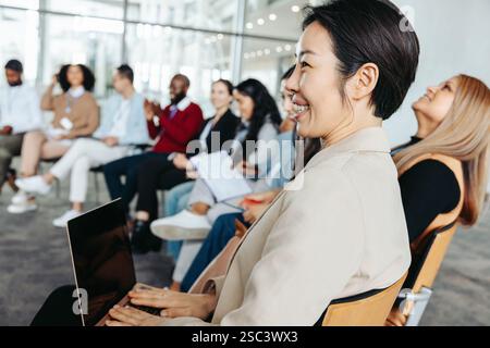 Eine lächelnde Geschäftsfrau, die während einer Geschäftspräsentation in einer vielfältigen Gruppenumgebung aufmerksam zuhört. Stockfoto
