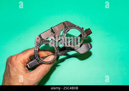 Weibliche Hände, die ein optisches Gerät zur Sehuntersuchung auf grüner Oberfläche halten. Stockfoto