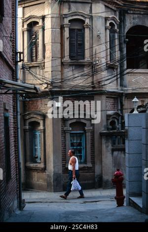 Ein Mann läuft an alten Ziegelgebäuden in Shanghai, China, vorbei und trägt eine Tasche in einem Stadtviertel. Stockfoto