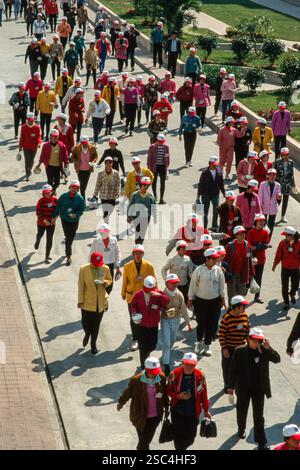 Eine große Gruppe junger Frauen Schuhfabrikarbeiter, die auf einem Weg spazieren gehen, viele tragen bunte Jacken und weiße Mützen mit roter Krempe. Stockfoto