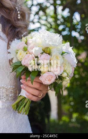 Die Braut hält einen Strauß aus weißen Pfingstrosen und weichen rosa Rosen in zarten Pastelltönen Stockfoto