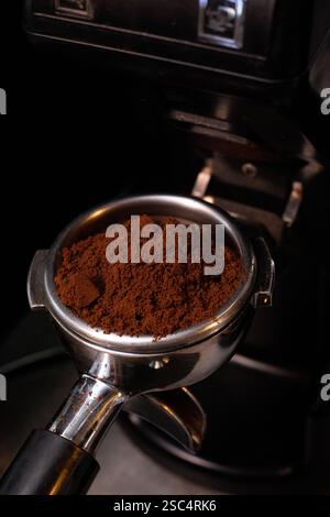 Nahaufnahme des Portafilters der Espressomaschine gefüllt mit frischem, dunkel geröstetem Kaffeesatz, bereit zum Brühen. Dunkle, dramatische Studioaufnahmen. Stockfoto