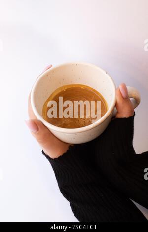 Weibliche Hände in einem schwarzen Pullover, der eine Tasse schwarzen Kaffees auf weißem Hintergrund hält. Gemütliches minimalistisches Tageskonzept am Morgen. Stockfoto