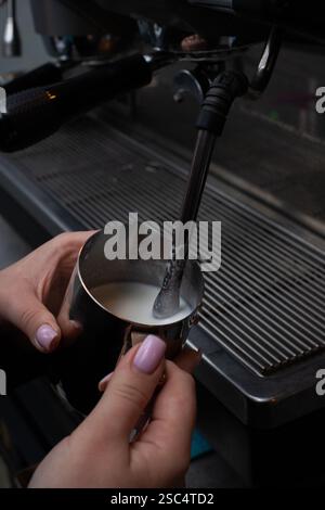 Nahaufnahme der Barista Hände, die Milch in einem Metallkrug mit einer Espressomaschine aufschäumen. Zubereitung von cremigem Milchschaum für Cappuccino oder Latte. Stockfoto