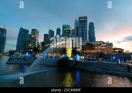 Dämmerung über dem Finanzviertel und dem Symbol von Singapur, dem „Merlion“, das Wasser auf der Marina Bay, Singapur, sprüht Stockfoto