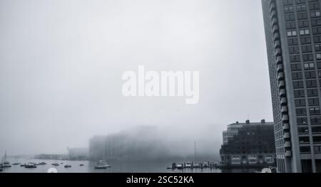 Ein nebeliger Morgen über dem Hafen von Boston mit Booten und Hochhäusern, die teilweise von Nebel verdeckt sind, schaffen eine stimmungsvolle urbane Uferszene. Stockfoto