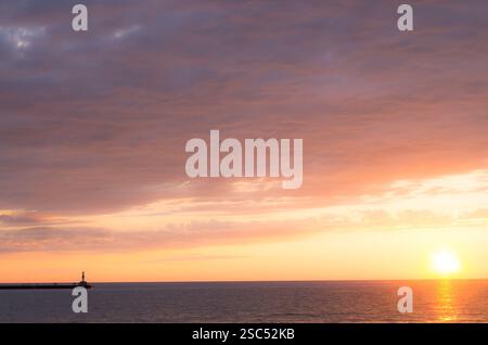 Ruhiger Sonnenuntergang über dem Lake Michigan mit einem Leuchtturm am Pier, der ein goldenes Licht auf das ruhige Wasser und den Himmel wirft. Stockfoto