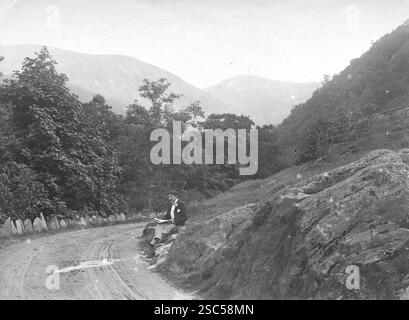 Ein Mann, der neben einer kurvenreichen Straße sitzt, die zu den ab Falls führt, auch bekannt als Rhaeadr Fawr in Walisisch, in der Nähe des Dorfes Abergwyngregyn, etwa 3 km südlich von Trefriw. Der Wasserfall wird durch den Afon Goch in den Ausläufern der Carneddau Mountains in Nordwales gebildet. 1900, monochrom: Aus einer bedeutenden historischen Sammlung von originalen, nicht zugeschriebenen Albumenfotos aus der späten viktorianischen bis frühen Edwardianischen Zeit: Eine britische Tour einschließlich Staffordshire, Warwickshire und Nordwales. Die Qualität der Originale war variabel und die meisten waren etwa 108 x 165 mm. Stockfoto
