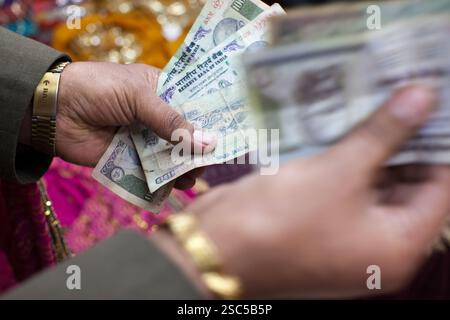 Hände, die Banknoten aus indischer Rupie halten und zählen, in einer lebhaften Marktplatzszene. Stockfoto