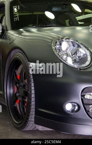 Eine Nahaufnahme eines dunklen, wahrscheinlich mattschwarzen Porsche 911 (oder eines ähnlichen Sportwagens). Das Auto ist auf einer Autoausstellung. Stockfoto