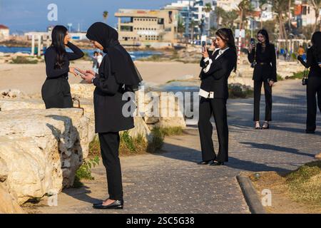 Eine Gruppe arabischer Mädchen in schwarzen Hosen und weißen Hemden macht Selfies vor dem Hintergrund des Meeres. Stockfoto