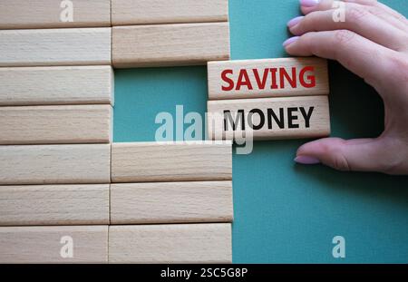 Symbol „Geld sparen“. Konzeptwort spart Geld bei Holzklötzen. Geschäftsmann Hand. Wunderschöner graugrüner Hintergrund. Business- und Sparkonzept. Stockfoto