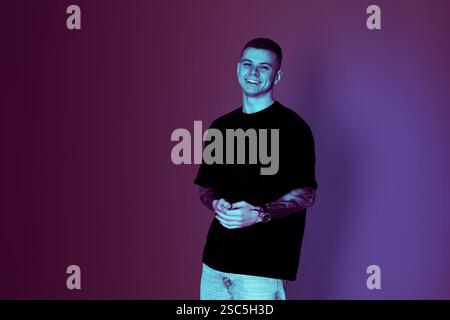 Lächelnder junger Mann mit Tätowierungen im Neonlicht, Raum für Text Stockfoto
