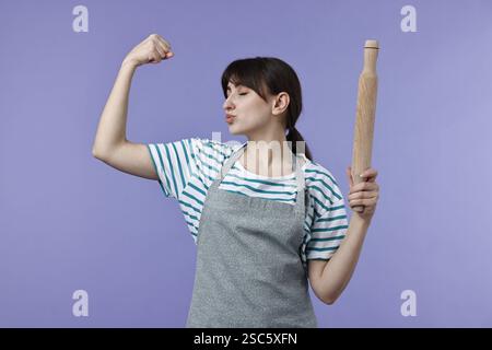 Frau mit rollendem Pin, der Bizeps auf violettem Hintergrund küsst Stockfoto