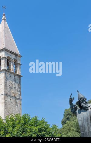 Eine ruhige Szene mit einem historischen Glockenturm neben einer hohen Statue, umgeben von üppigem Grün, unter einem klaren blauen Himmel, der an Kultur und Geschichte erinnert Stockfoto