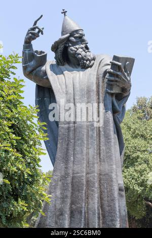 Eine ruhige Szene mit einem historischen Glockenturm neben einer hohen Statue, umgeben von üppigem Grün, unter einem klaren blauen Himmel, der an Kultur und Geschichte erinnert Stockfoto