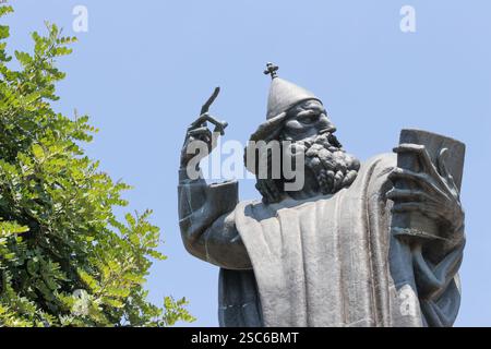 Eine ruhige Szene mit einem historischen Glockenturm neben einer hohen Statue, umgeben von üppigem Grün, unter einem klaren blauen Himmel, der an Kultur und Geschichte erinnert Stockfoto
