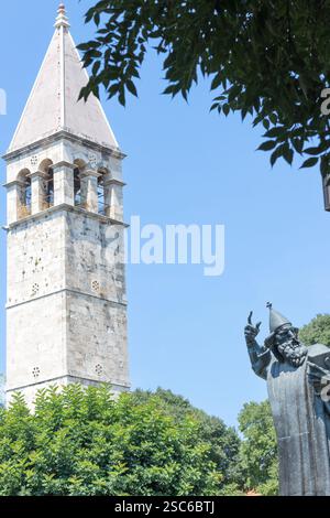 Eine ruhige Szene mit einem historischen Glockenturm neben einer hohen Statue, umgeben von üppigem Grün, unter einem klaren blauen Himmel, der an Kultur und Geschichte erinnert Stockfoto