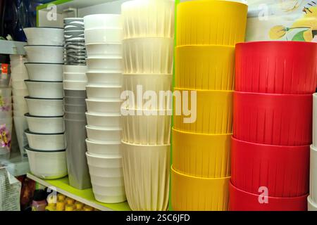 Plastikblumentöpfe in einem Regal in einem Blumenladen. Verschiedene Farben und Formen: Weiße, graue, beige, gelbe und rote Töpfe zum Pflanzen. Stockfoto