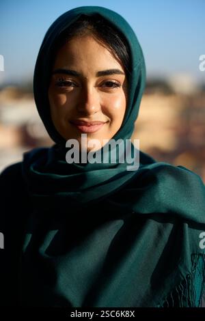 Junge muslimische Frau lächelt und trägt Hijab in urbaner Umgebung Stockfoto