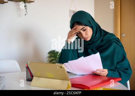 Gestresste muslimische Geschäftsfrau liest Dokumente im Home Office Stockfoto