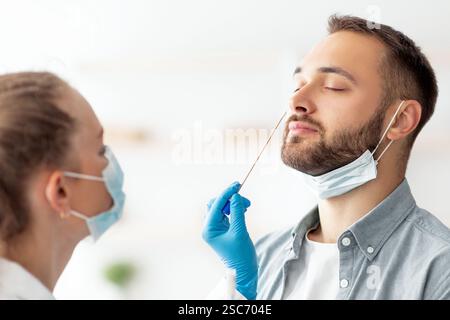 Ärztin, die in der Klinik einen nasalen Coronavirus-PCR-Test für einen Tausendjährigen Mann macht. Konzept zum Schutz von Infektionskrankheiten Stockfoto