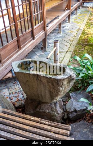 Steinwasserbecken und Bambusbrunnen in einem traditionellen japanischen Garten, umgeben von Holzarchitektur Stockfoto