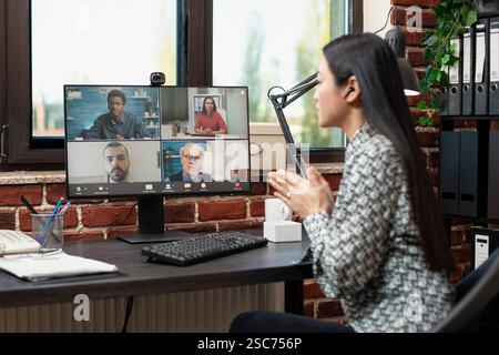 Asiatische Geschäftsfrau auf Videokonferenz, die mit ihrem Team Geschäftsprojektpläne diskutiert. Der Desktop-Monitor zeigt ein virtuelles Meeting, bei dem eine Führungskraft Strategievorschläge mit ihren Remote-Mitarbeitern teilt. Stockfoto