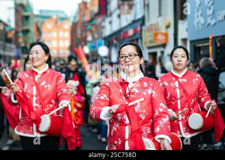 Drei asiatische Frauen in roter traditioneller chinesischer Kleidung spielen bei einer festlichen Parade in einer überfüllten Stadtstraße Trommeln. Stockfoto