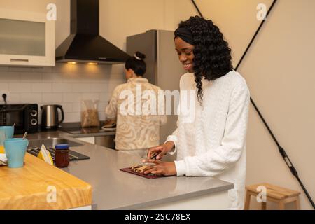 Eine junge Frau schneidet frisches Gemüse und bereitet ein köstliches Frühstück in einer modernen Küche zu, während ihr Freund auf dem Herd kocht und einen gemütlichen Morgen schafft Stockfoto