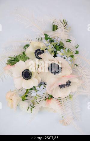 Ein atemberaubendes Arrangement aus weißen Anemonen mit dunklen Zentren, sanften rosa Blüten und zartem Grün liegt vor einem hellen Hintergrund und zeigt natürliche Ele Stockfoto