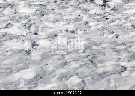 Eine detaillierte Nahaufnahme einer schneebedeckten Oberfläche, die unter hellem Tageslicht aufgenommen wurde. Das Bild zeigt eine komplexe Auswahl an verschneiten Texturen und Mustern, e Stockfoto