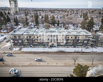 Großes Apartmenthaus mit vielen Fenstern und ein paar Autos auf der Straße unten. Der Himmel ist bewölkt und der Schnee fällt Stockfoto