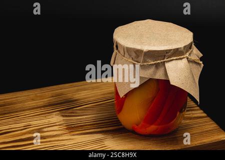 Auf einem Holztisch steht ein Glas mit hausgemachten, eingelegten Paprika. Der Becher ist mit einem Papierdeckel und Garn versiegelt, was die traditionelle Stockfoto
